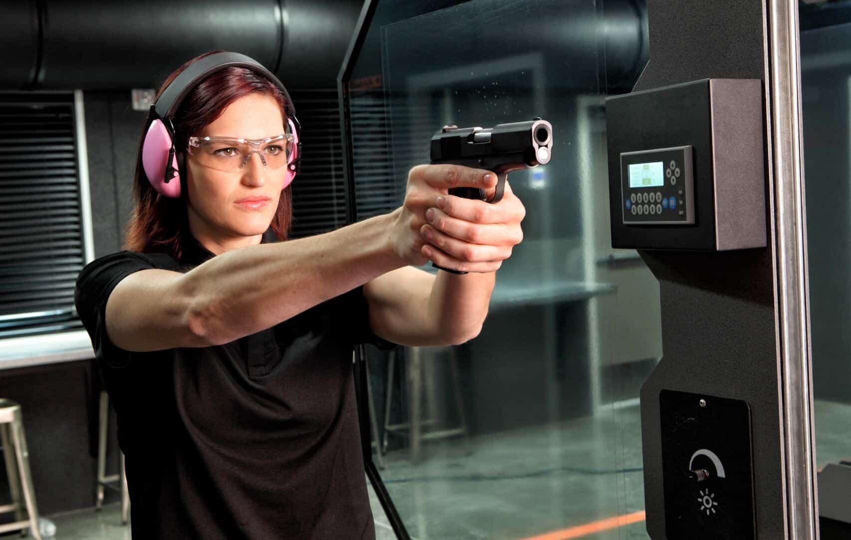 Femme-avec-des-lunettes-de-securite-et-un-casque-qui-tir-avec-un-pistolet-dans-stand-indoor